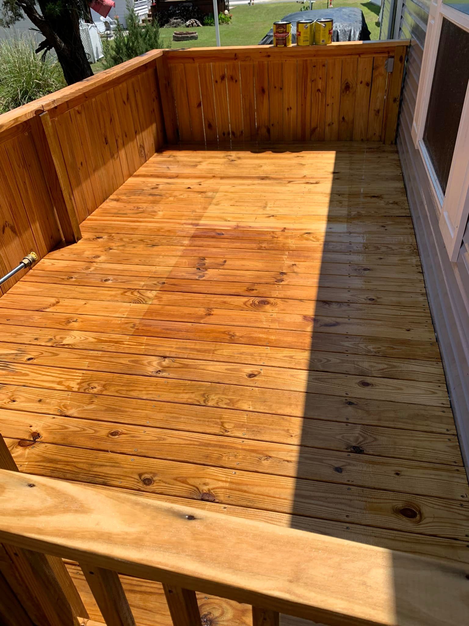 Sunlit wooden deck with railings and a ramp-like walkway beside a house