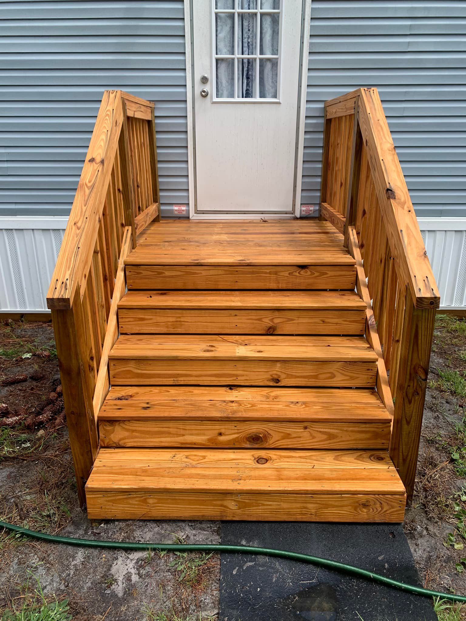 Wooden front steps and railings leading to a white door on a gray-sided house
