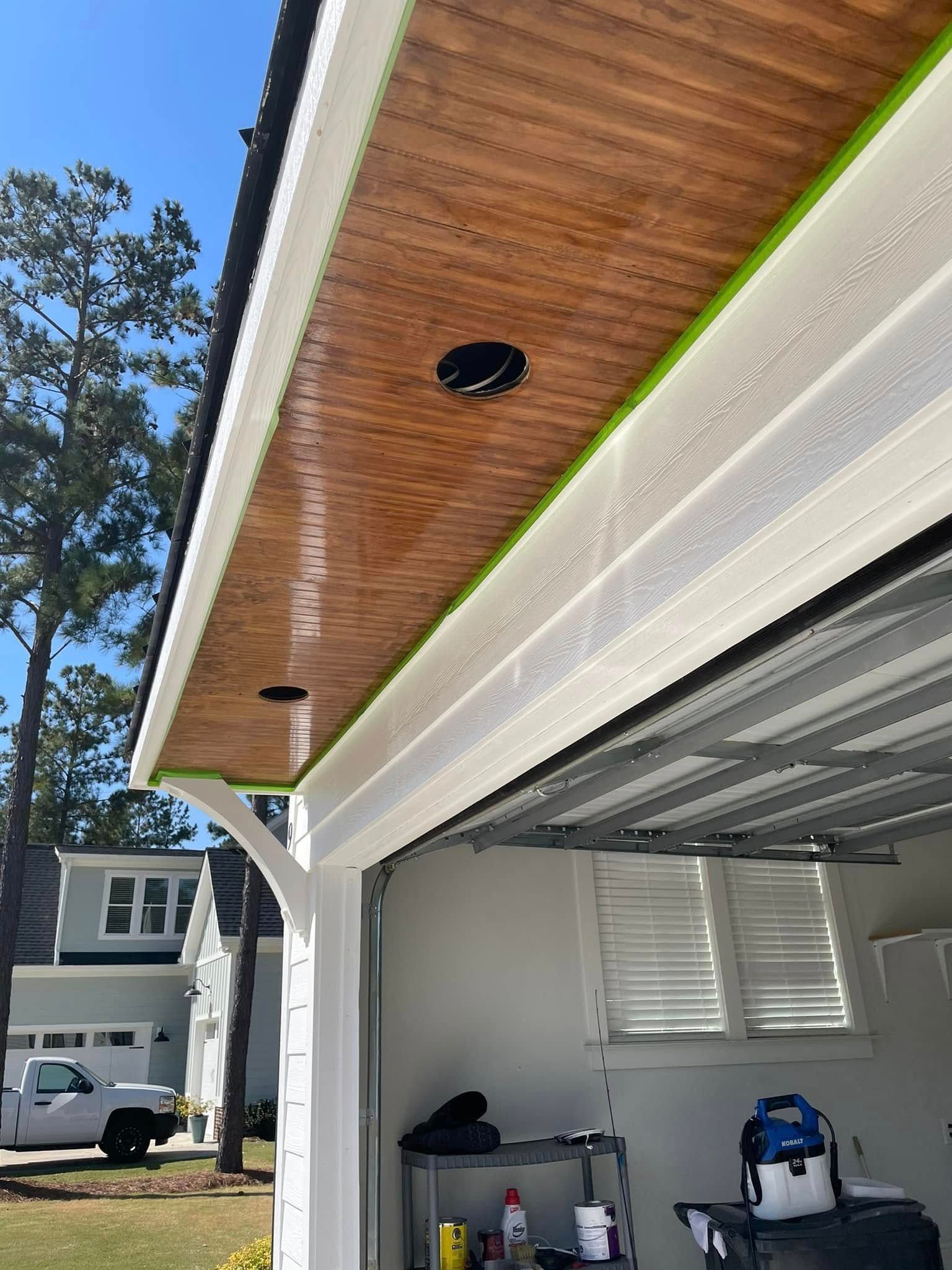 Open garage with wood-paneled soffit, recessed lights, and tools inside; house and trees visible outside