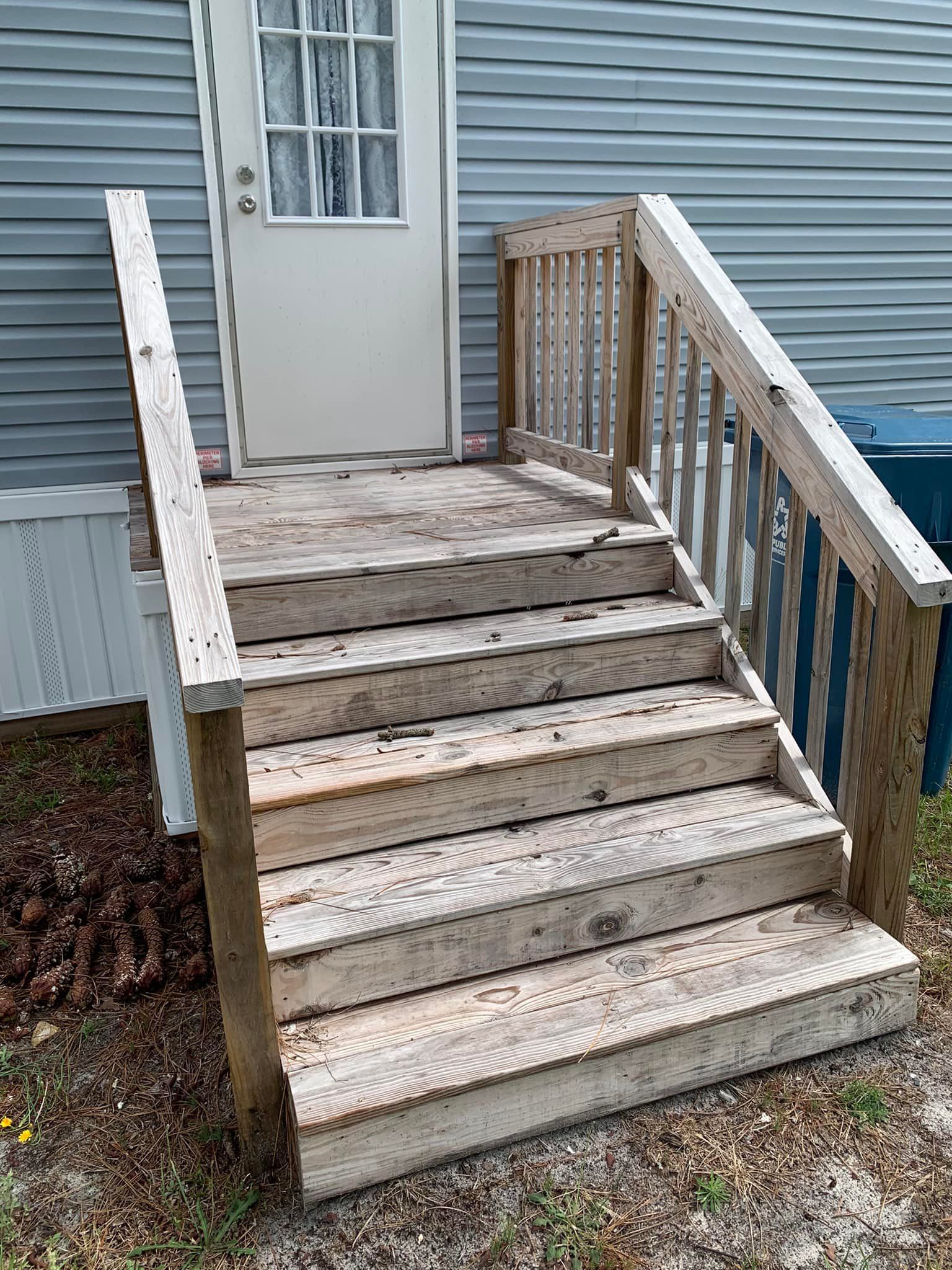 Weathered wooden steps and railing leading to a white door on a blue house porch.