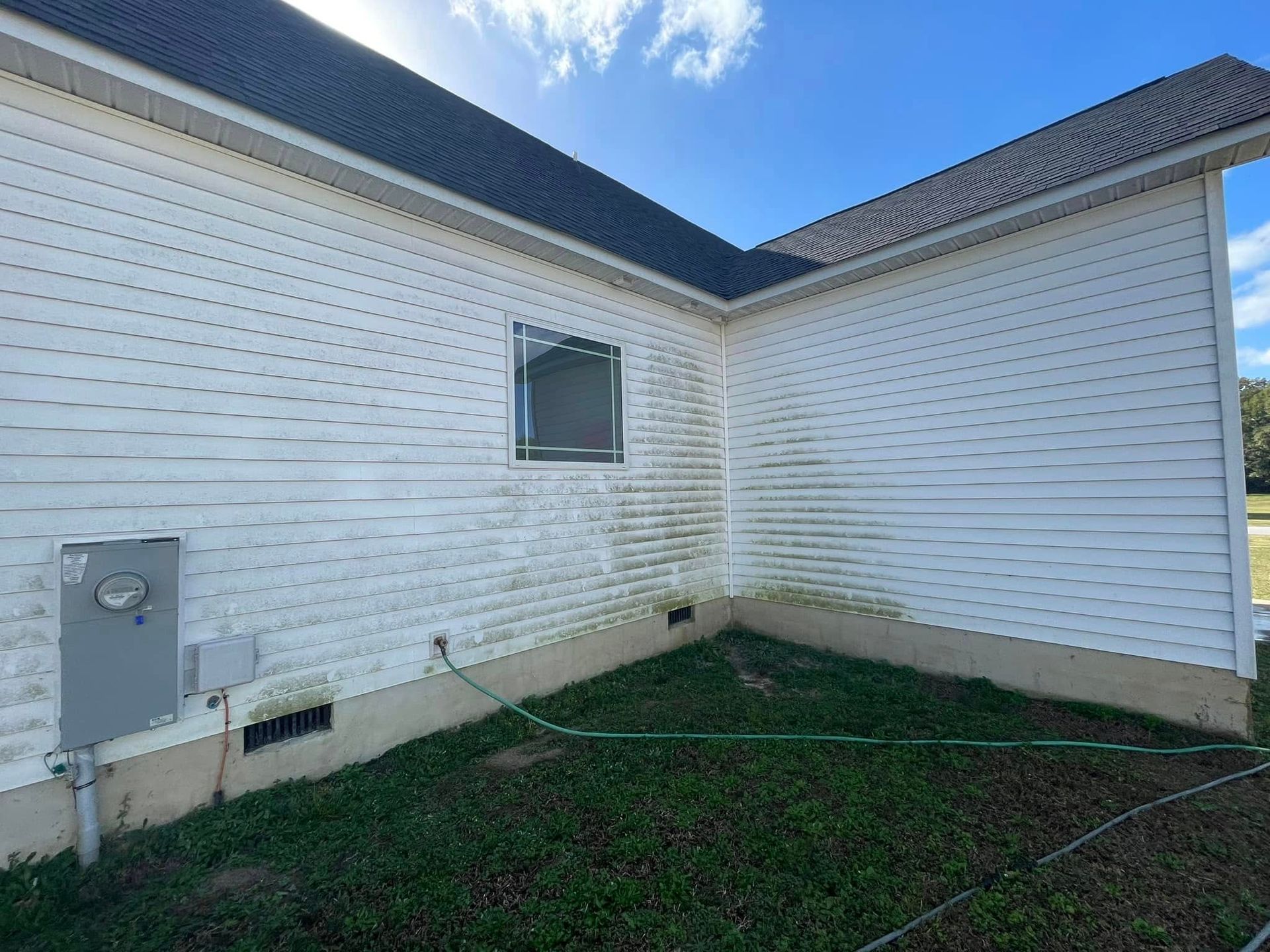 White house exterior corner with small window, utility meter, and grassy yard under a blue sky