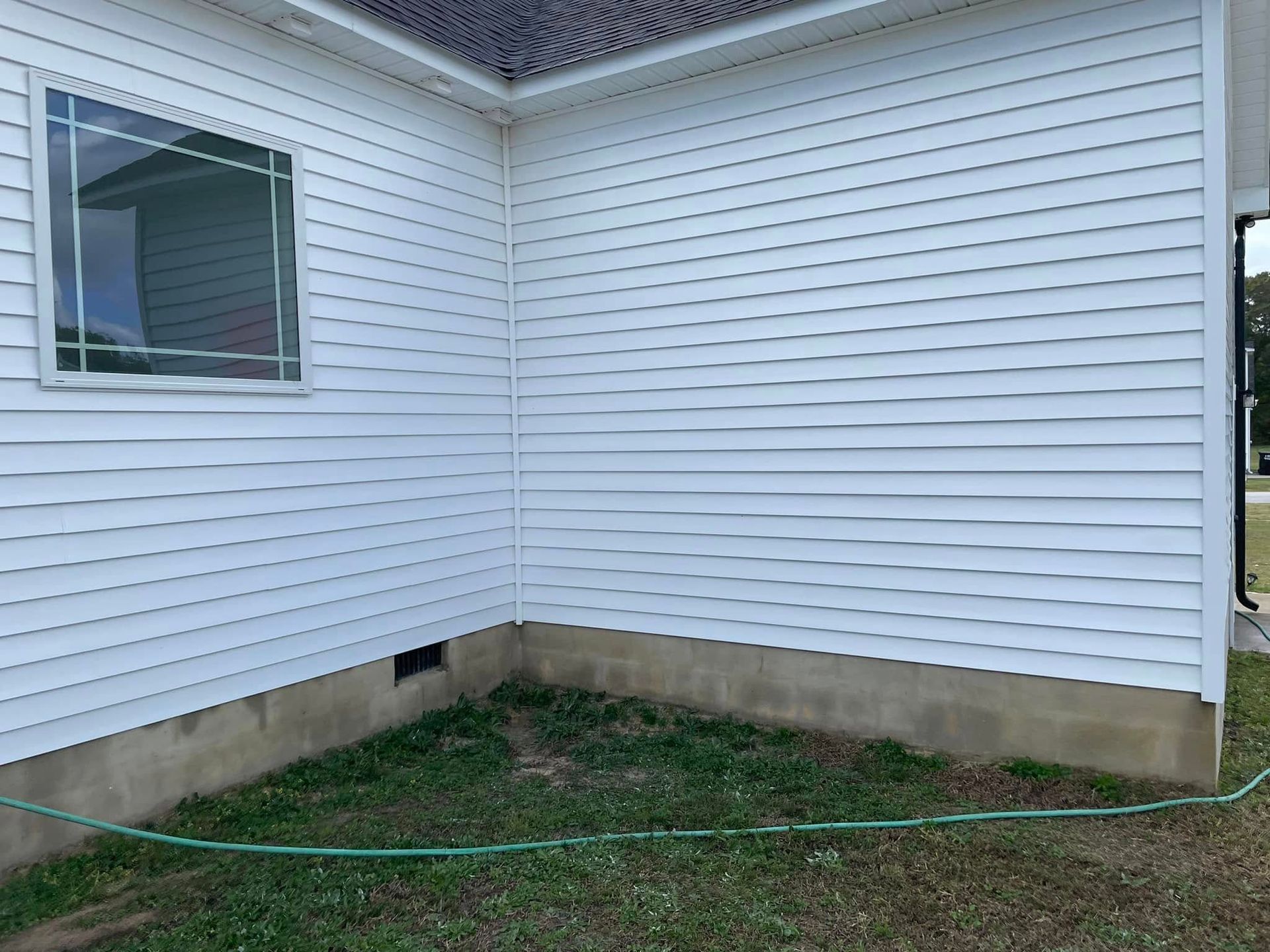 Corner of a house with white siding, a window, and a grassy yard bordered by a concrete foundation.