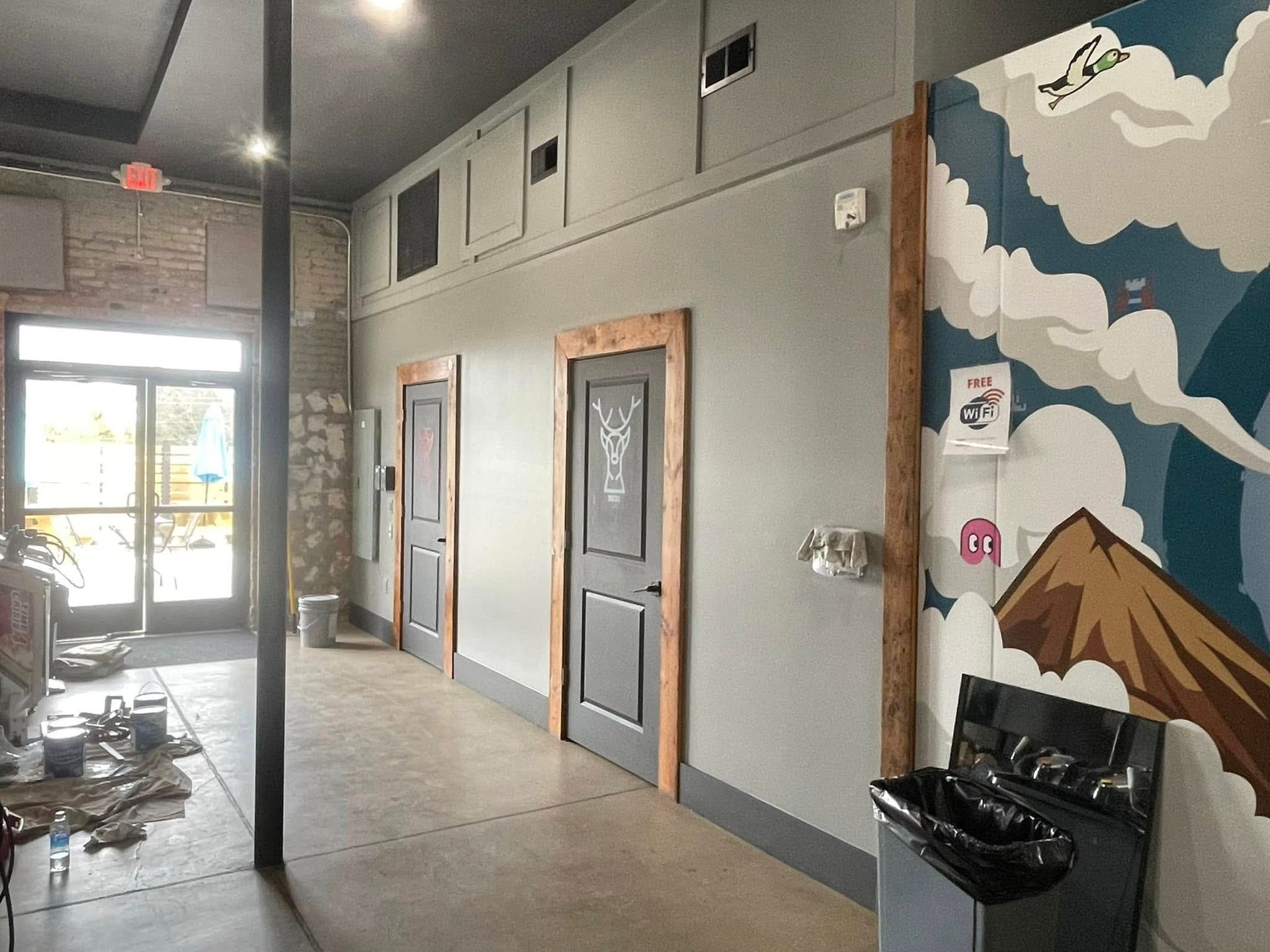 Indoor hallway with gray walls, doors, a black sink, and a colorful mountain mural by the entrance.
