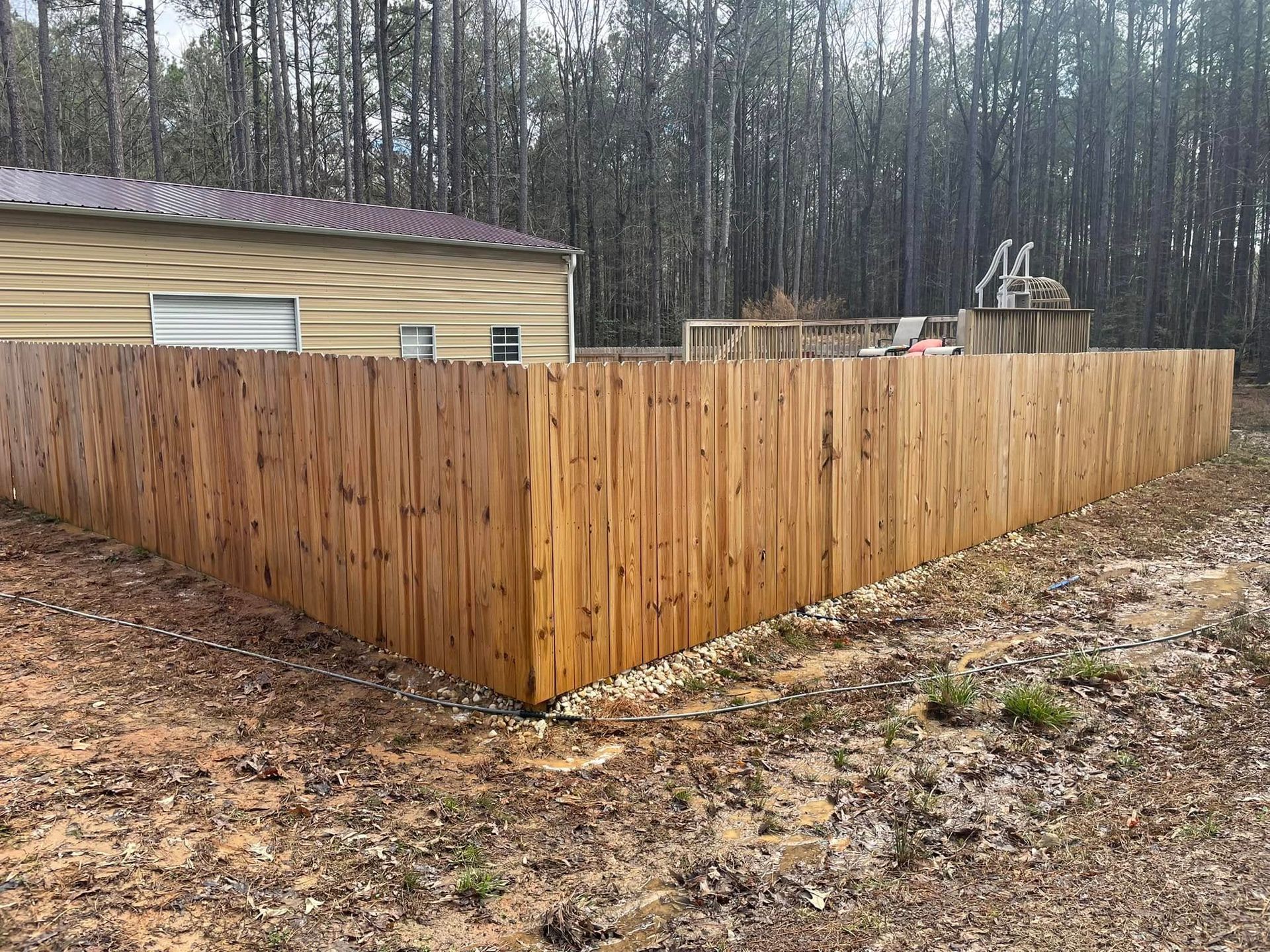 Wooden privacy fence corner beside a tan house in a wooded yard