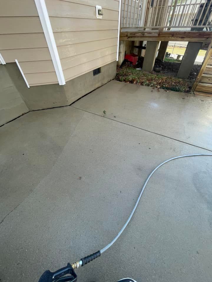 Concrete patio beside a beige house, with a gray hose stretched across the ground.