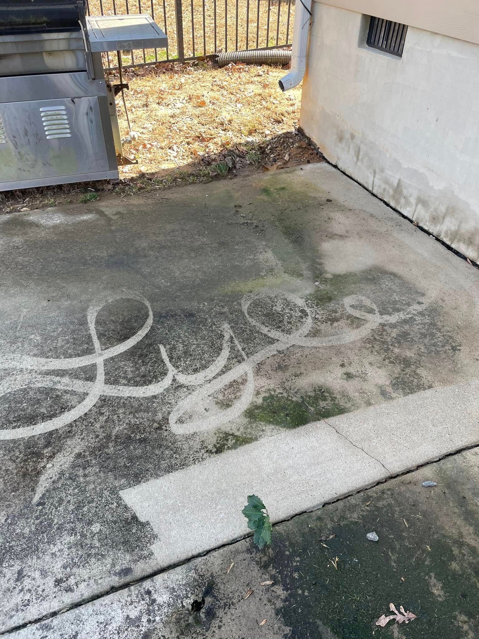Concrete patio with white chalk scribbles beside a house and trash bins, bordered by a fence and dry leaves.