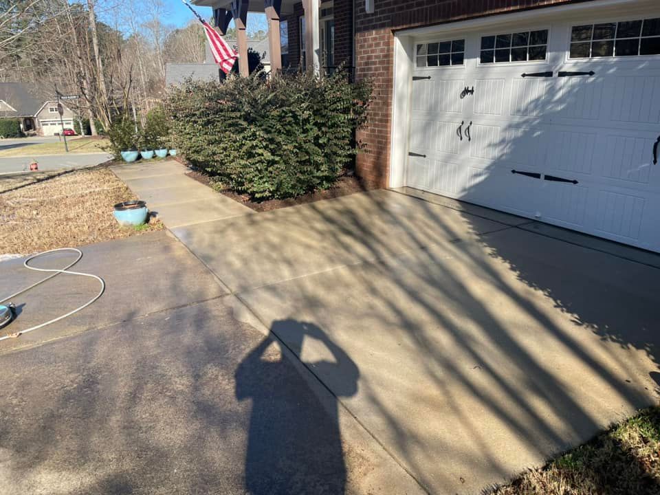 Driveway beside a garage with a bush, hanging American flag, and a long shadow on the pavement
