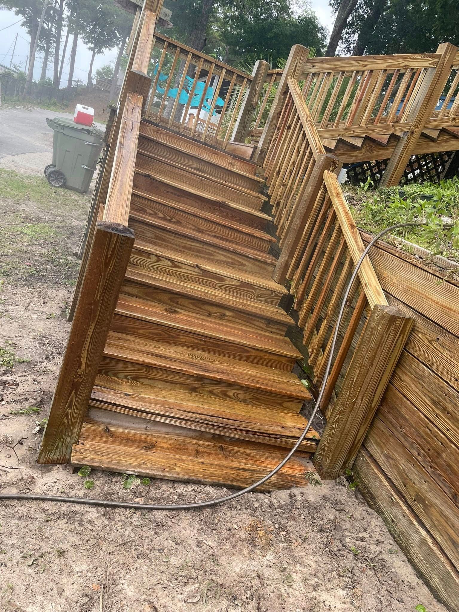 Wooden staircase on a tilted structure outdoors, with a cable lying across the gravel path.