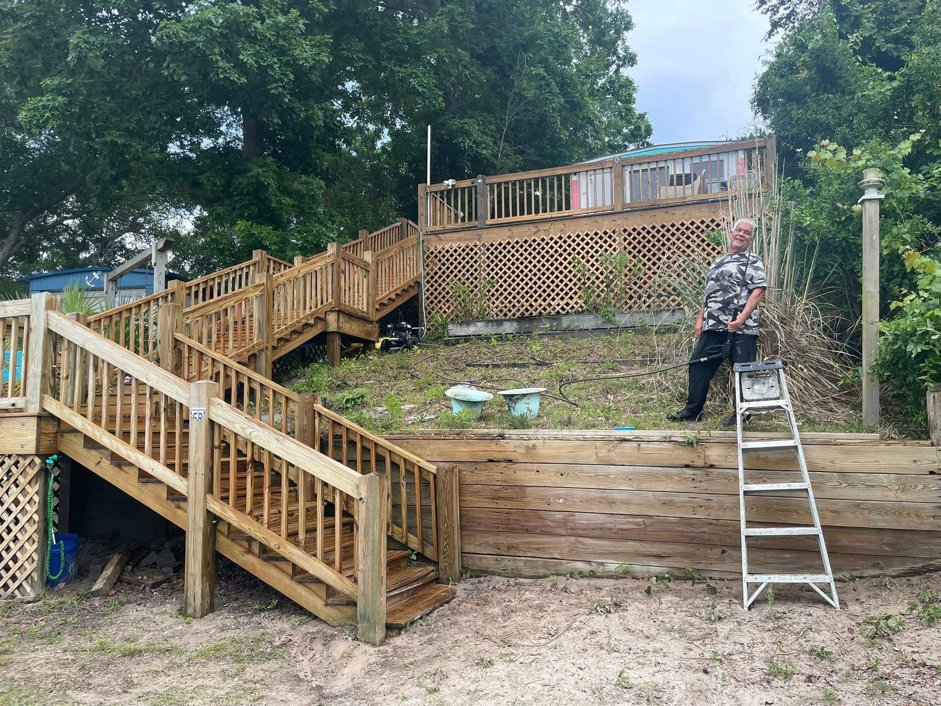 Wooden backyard deck and stairs under construction, with a person standing on a ladder.