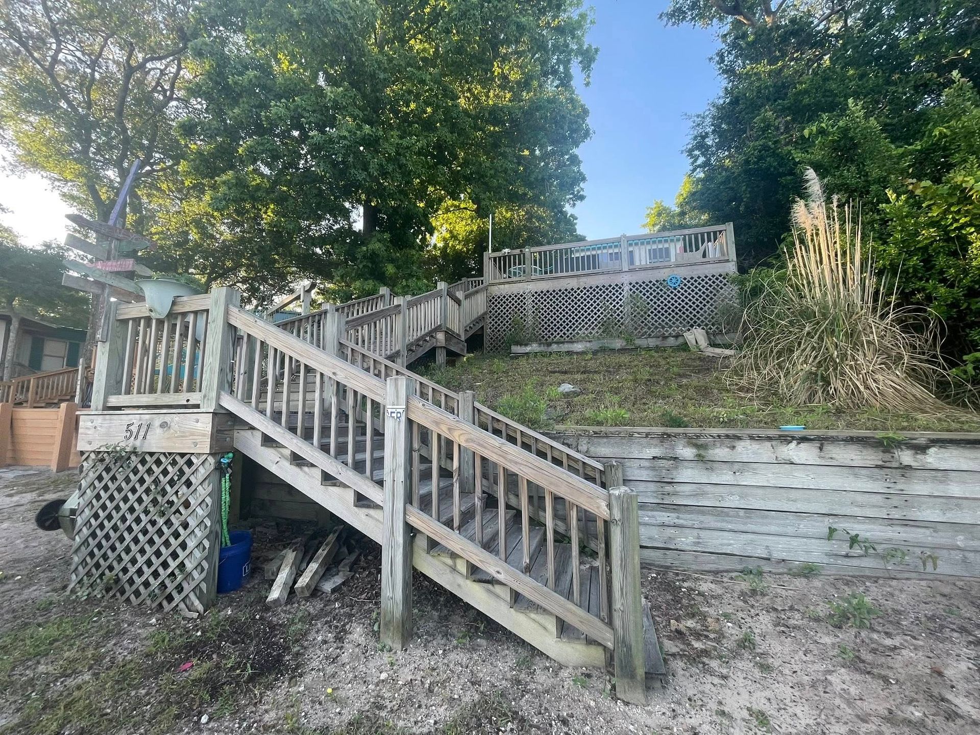 Steep wooden stairs with railing leading up a terraced yard beside a retaining wall and trees