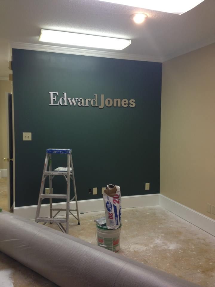 Empty office room with dark green Edward Jones wall, ladder, and paint supplies on the floor