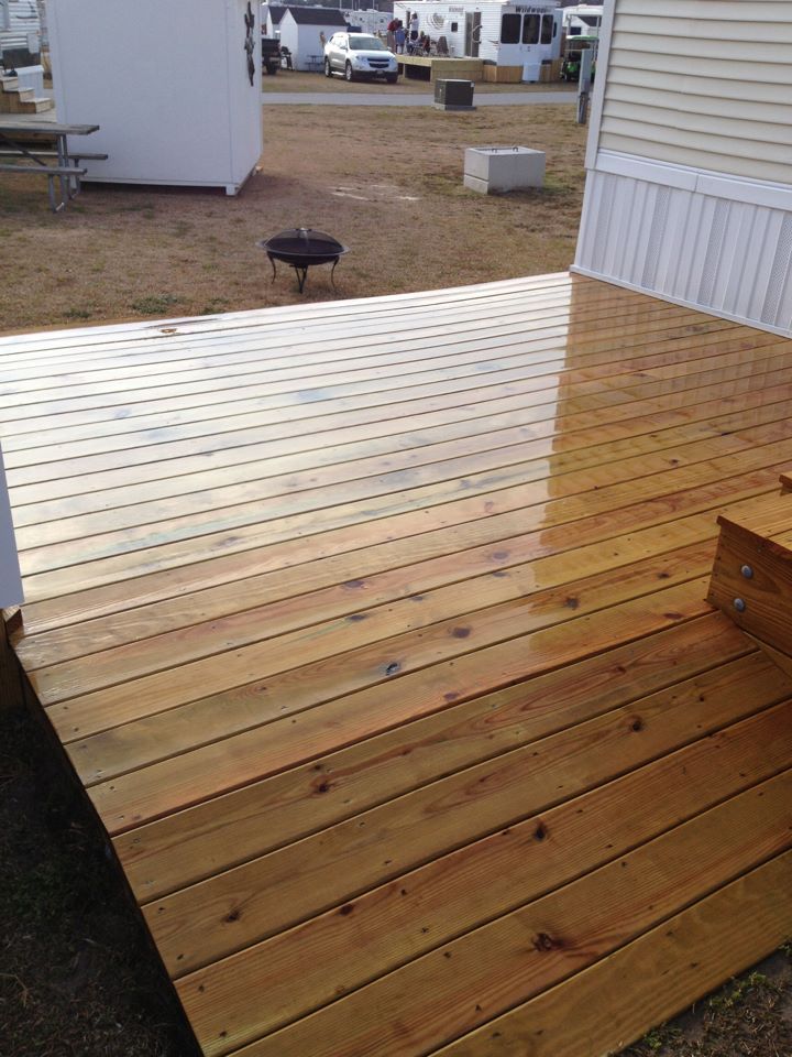 Freshly stained wooden deck with a wet, reflective section beside a beige house.