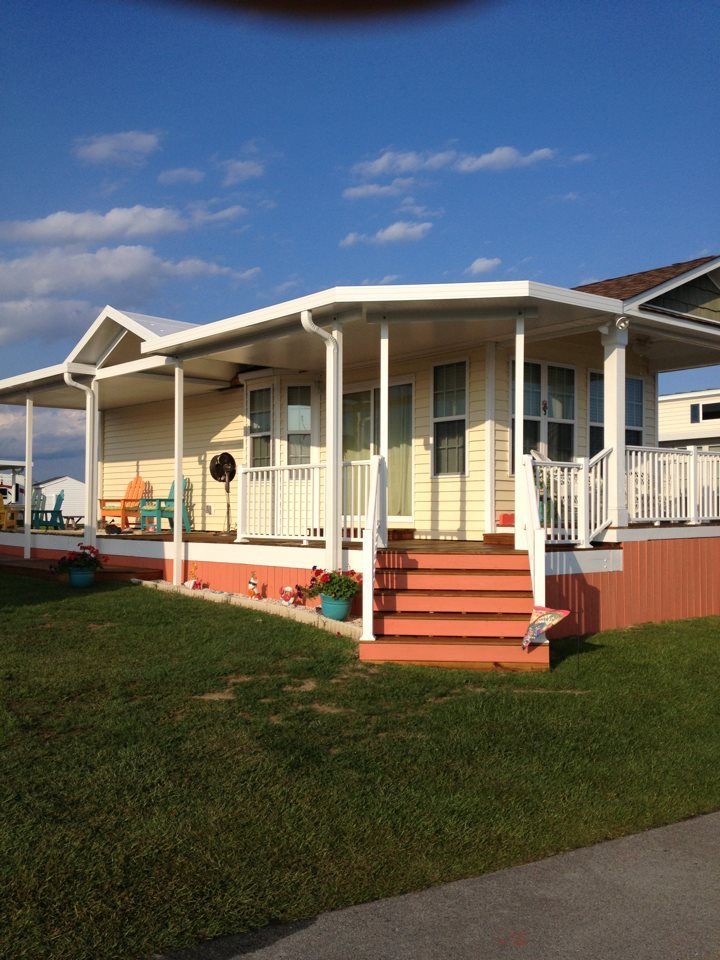 Single-story beige house with white porch columns, red steps, and green lawn under a blue sky.