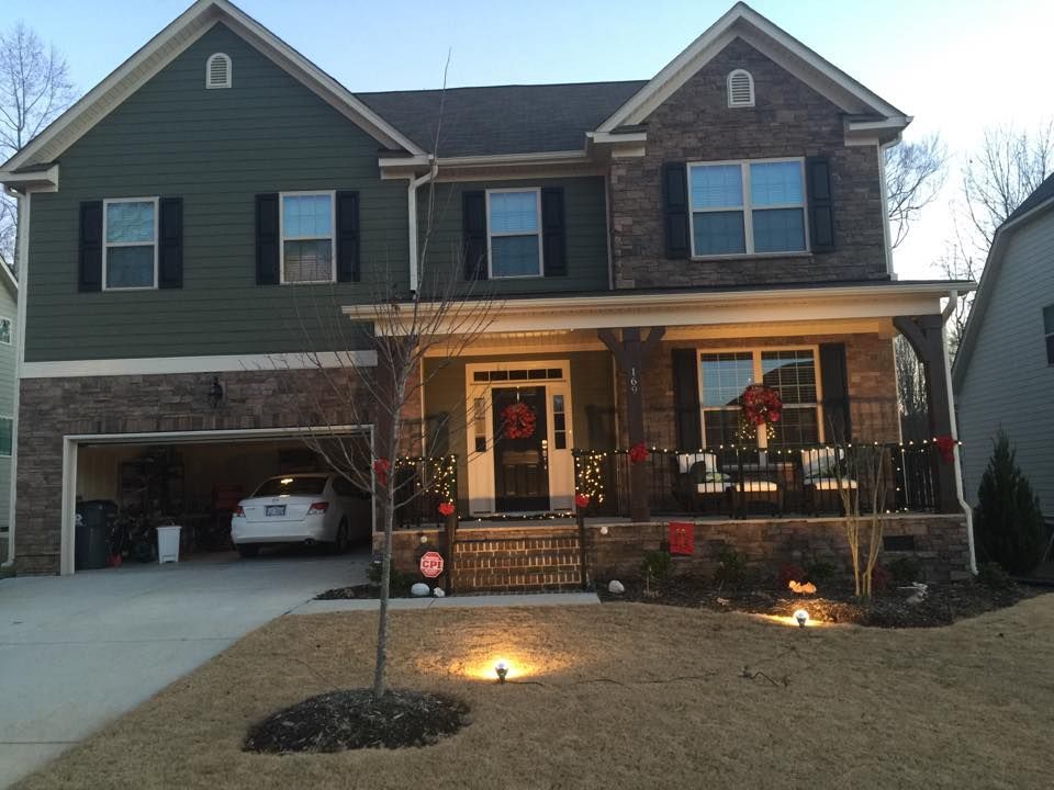 Two-story house with a lit front porch, car in garage, and a small front lawn at dusk