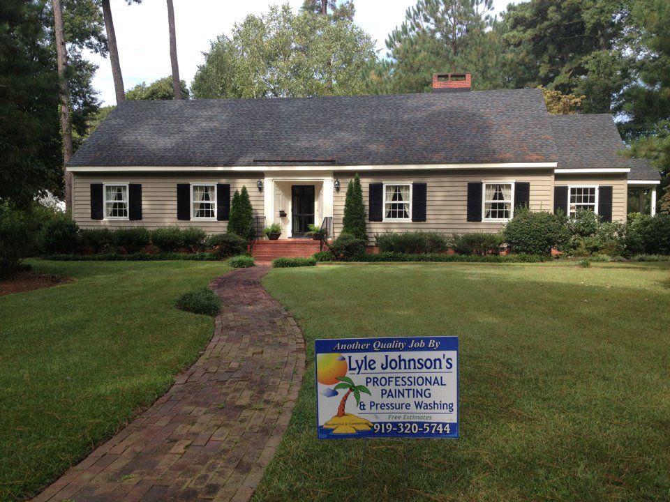 Single-story house with a brick walkway and a lawn sign advertising roofing services.