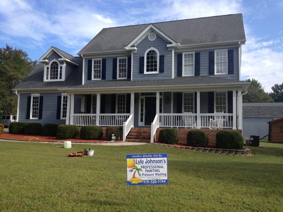 Large blue two-story house with white trim, front porch, and a lawn sign in the yard.