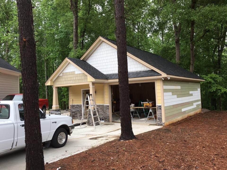 House under construction with ladder, open garage, and a pickup truck in a wooded driveway