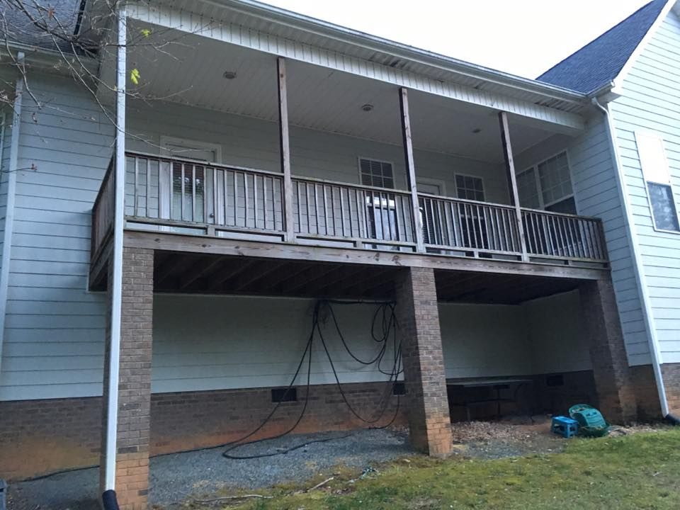 Back porch of a house with a roof, railing, brick support column, and items stored underneath