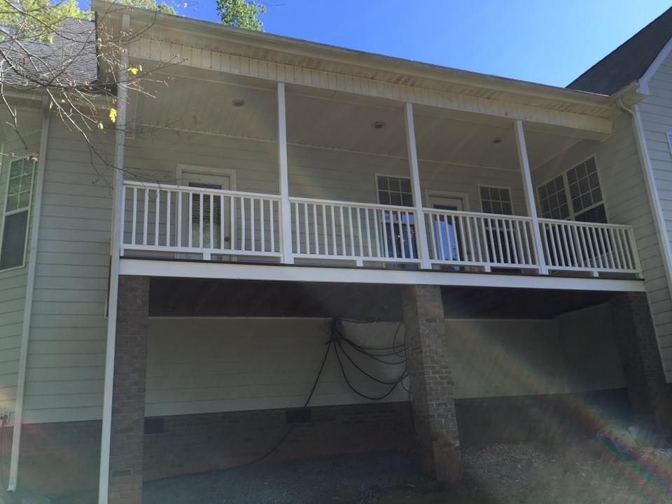 White elevated porch with white railings above a shaded carport on a house exterior