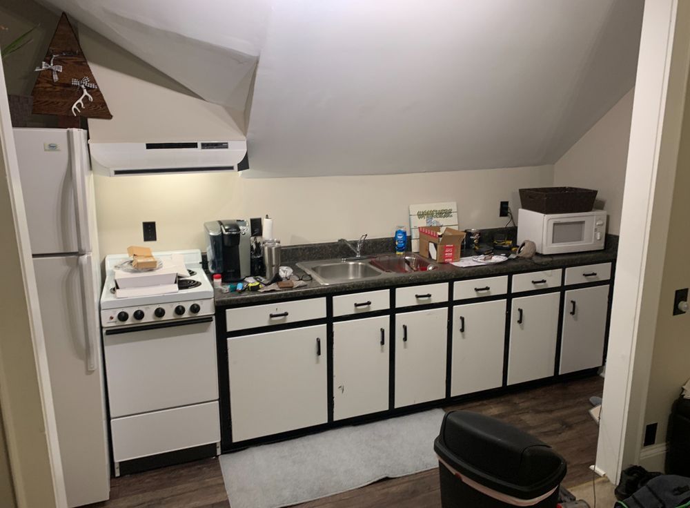 Small kitchen with white cabinets, stove, coffee maker, sink, and countertop appliances under a slanted ceiling