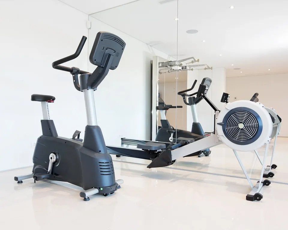 A gym with a bicycle , elliptical , and rowing machine.