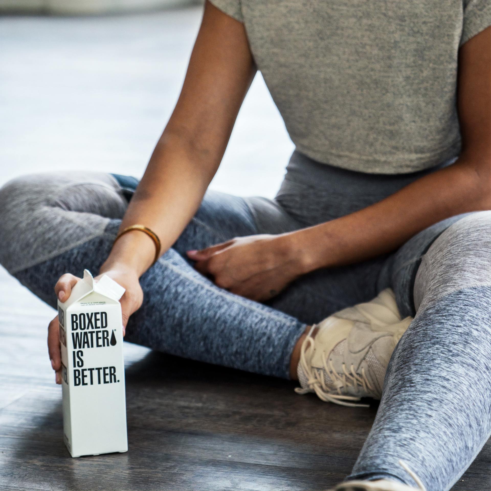 A woman is sitting on the floor holding a boxed water bottle