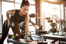 A woman is lifting a dumbbell on a bench in a gym.
