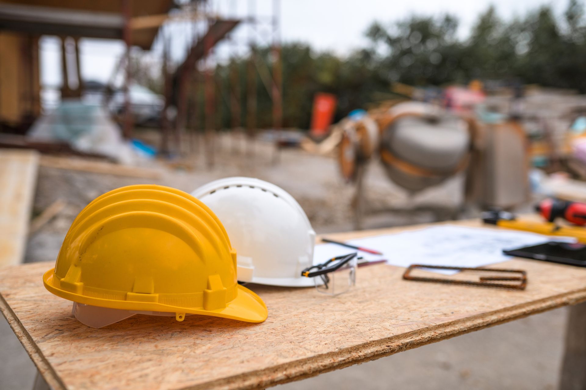 Due caschi di protezione e occhiali di sicurezza sono appoggiati su un tavolo di legno in un cantiere edile.