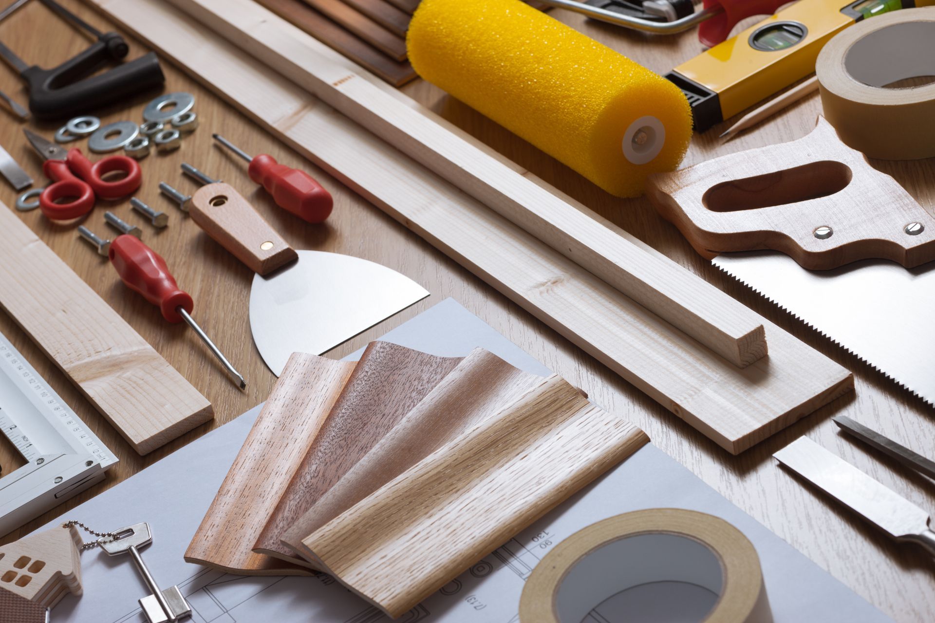 Vari utensili e materiali da falegnameria su una superficie di legno, tra cui una sega, un rullo e campioni di legno.