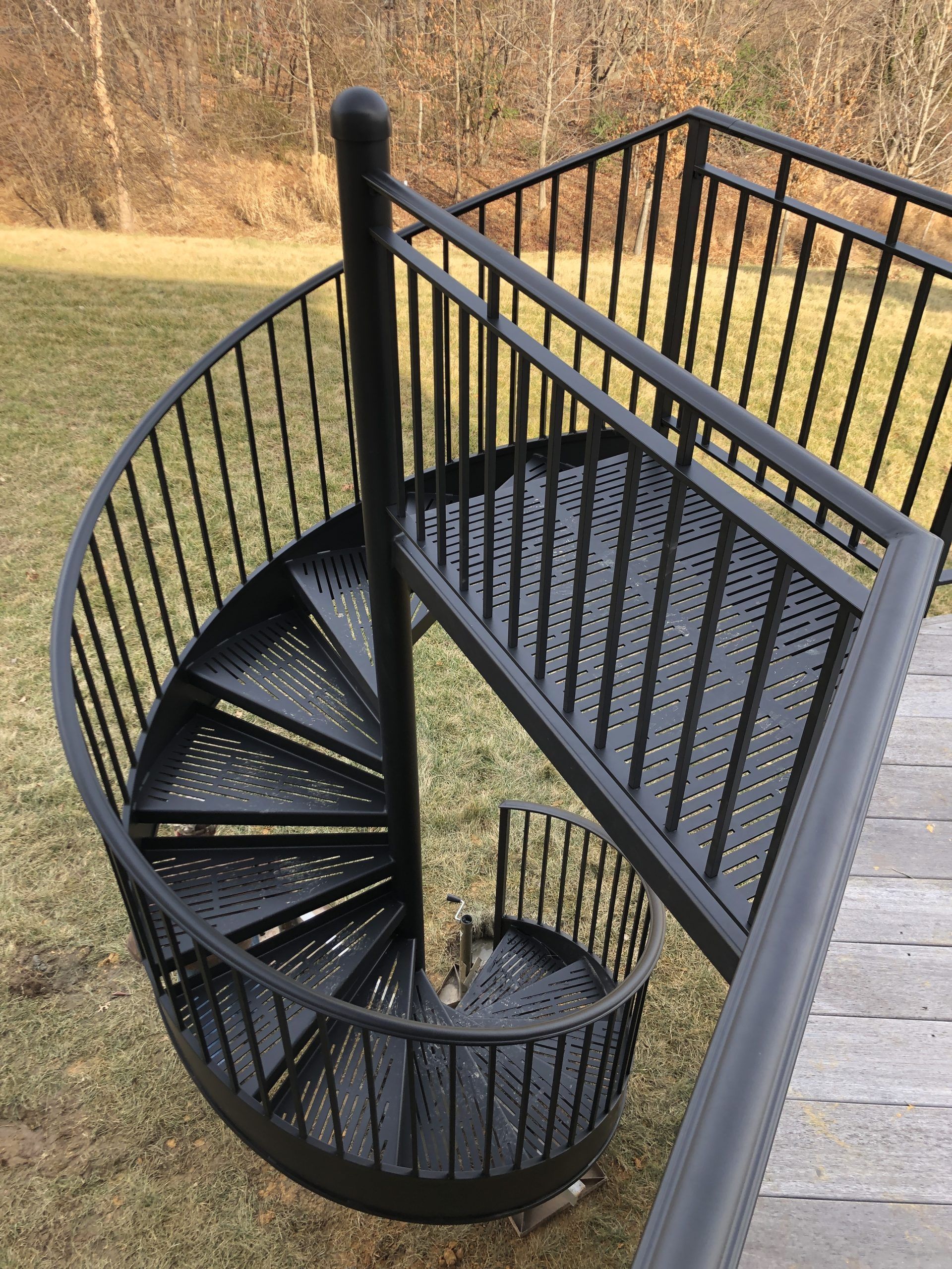 Black spiral staircase outdoors, leading to a wooden deck with railing.