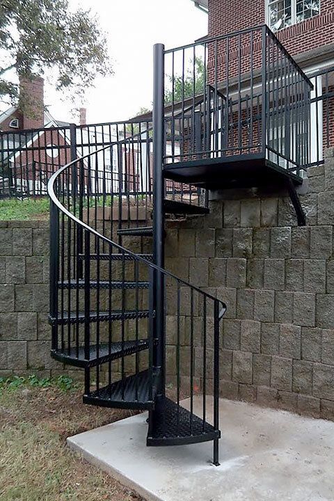 Black spiral staircase against a brick retaining wall leading to a balcony.