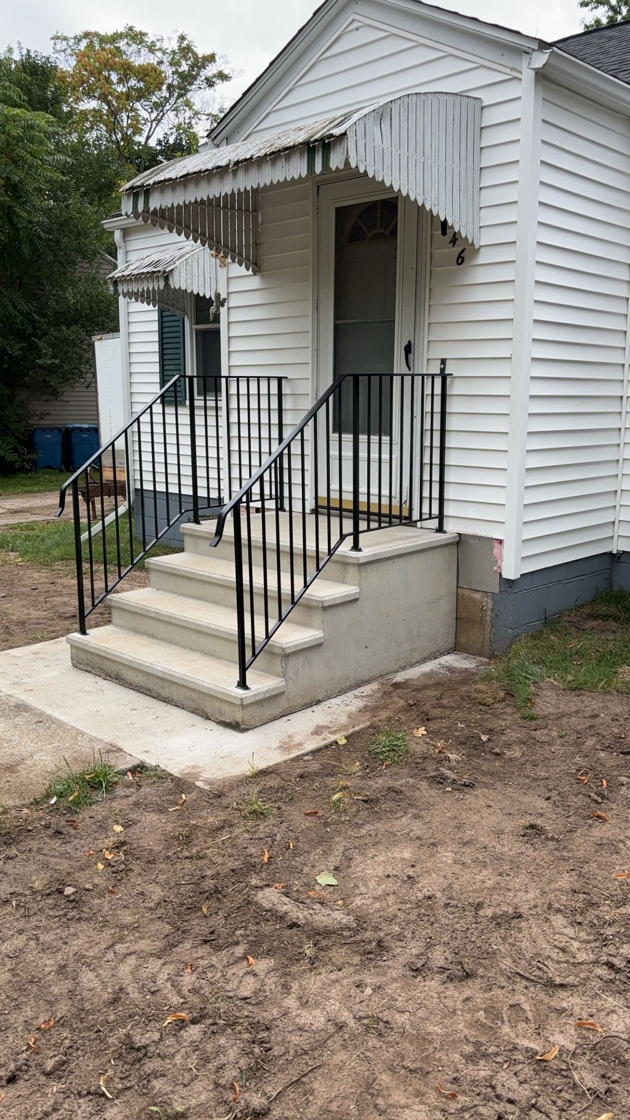 White house with concrete steps, black railing, and awning over the door.