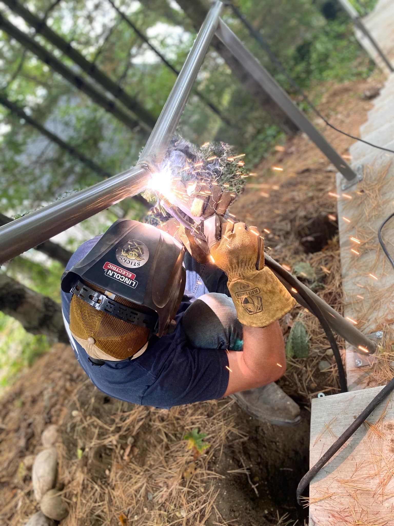 Welder wearing a helmet welding metal beams outdoors. Sparks fly from the joint.