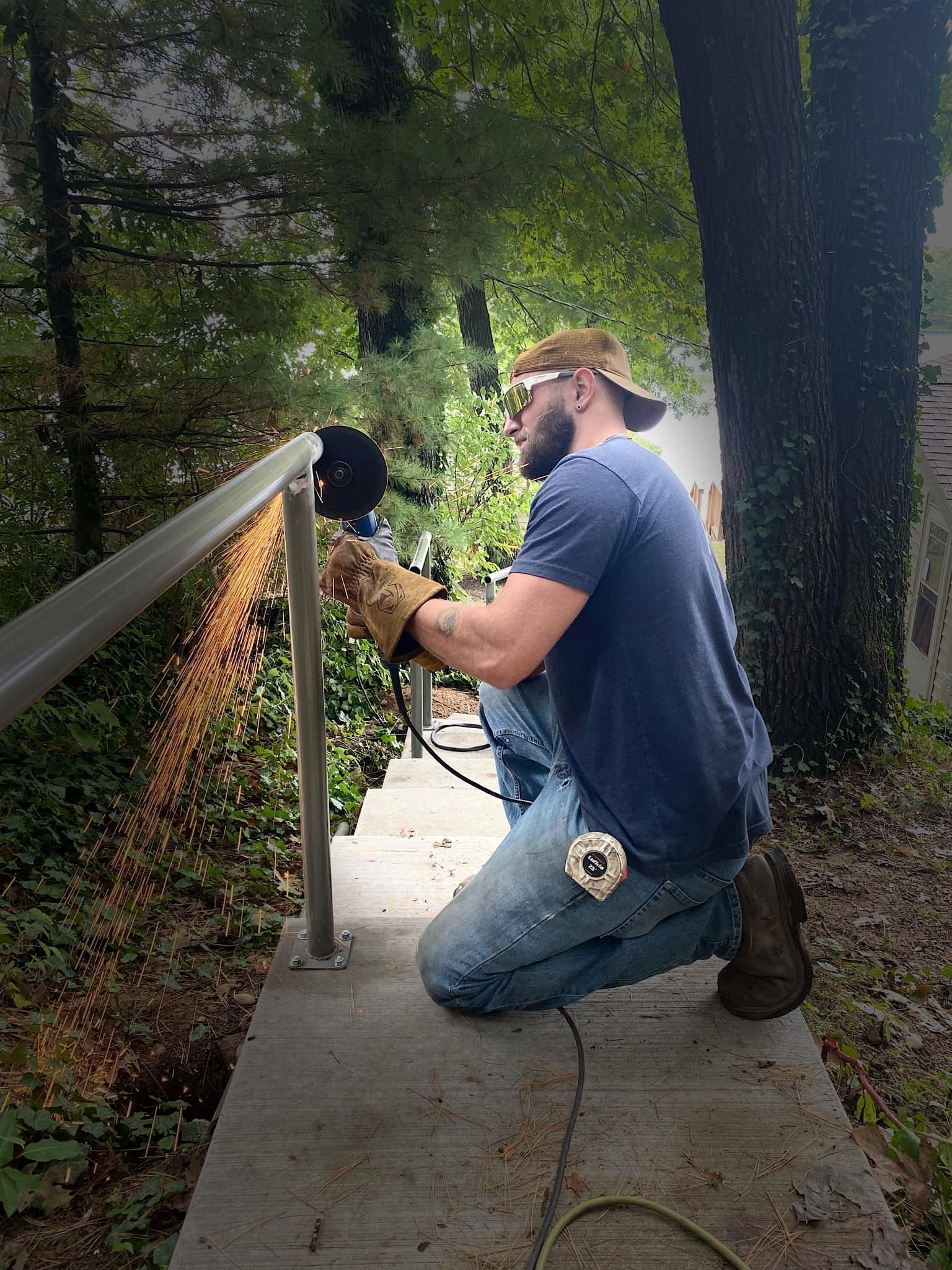 Person using a grinder on metal railing outdoors, kneeling with protective gear, sparks flying.