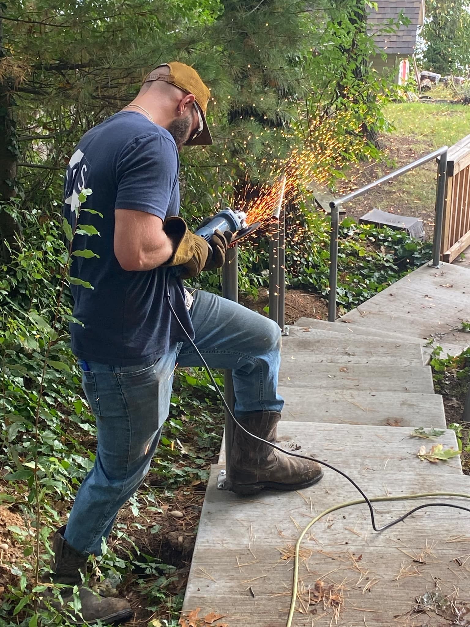 Man welding metal railing on outdoor concrete steps, sparks flying.