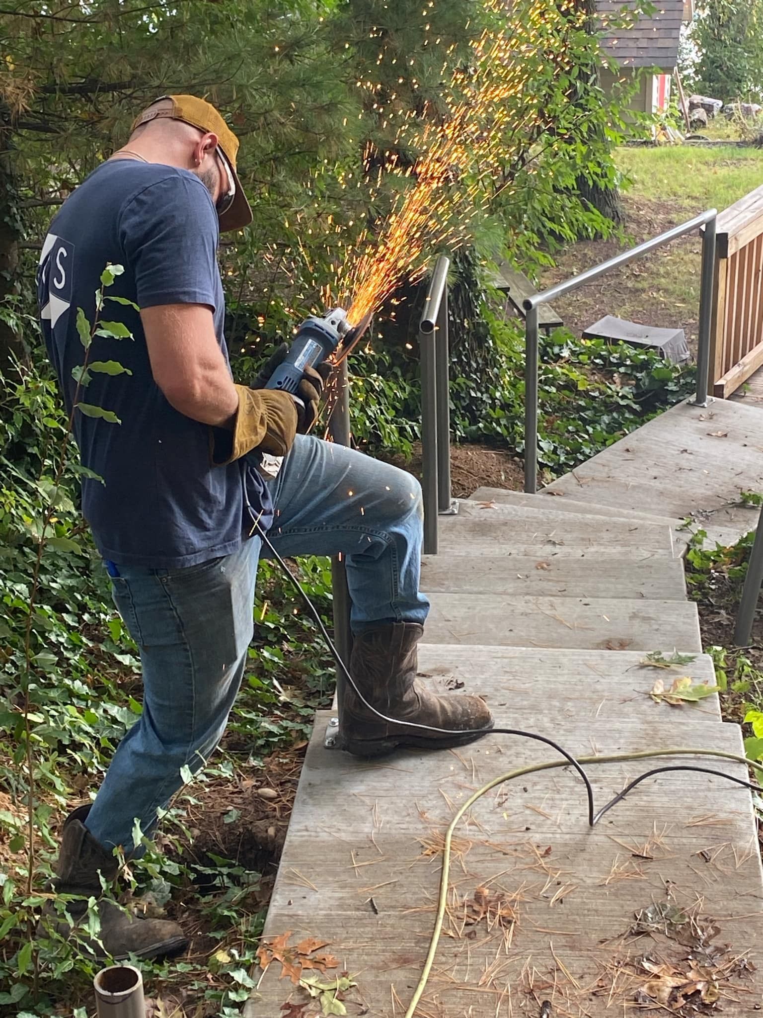 Man using a saw to cut metal railing on outdoor stairs, sparks flying.