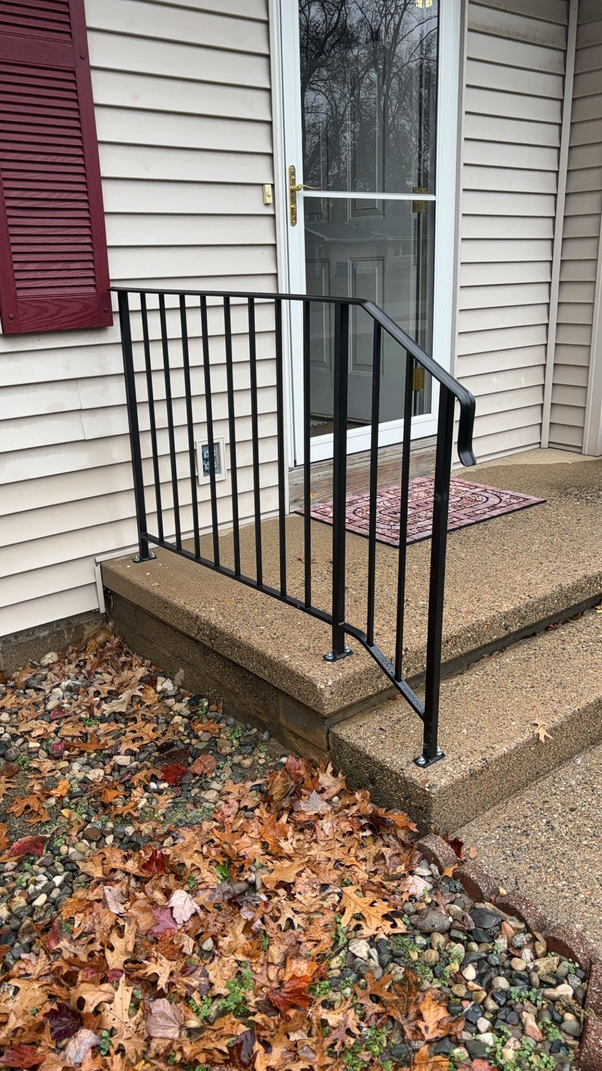 Exterior view of a house's entrance with a concrete staircase, black handrail, and fallen leaves.