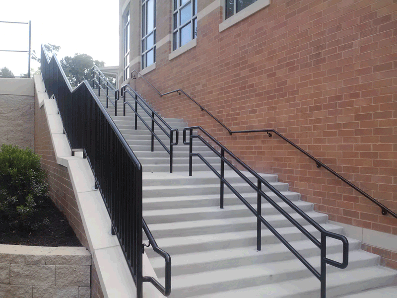 Outdoor concrete staircase with black handrails leading up a brick building.