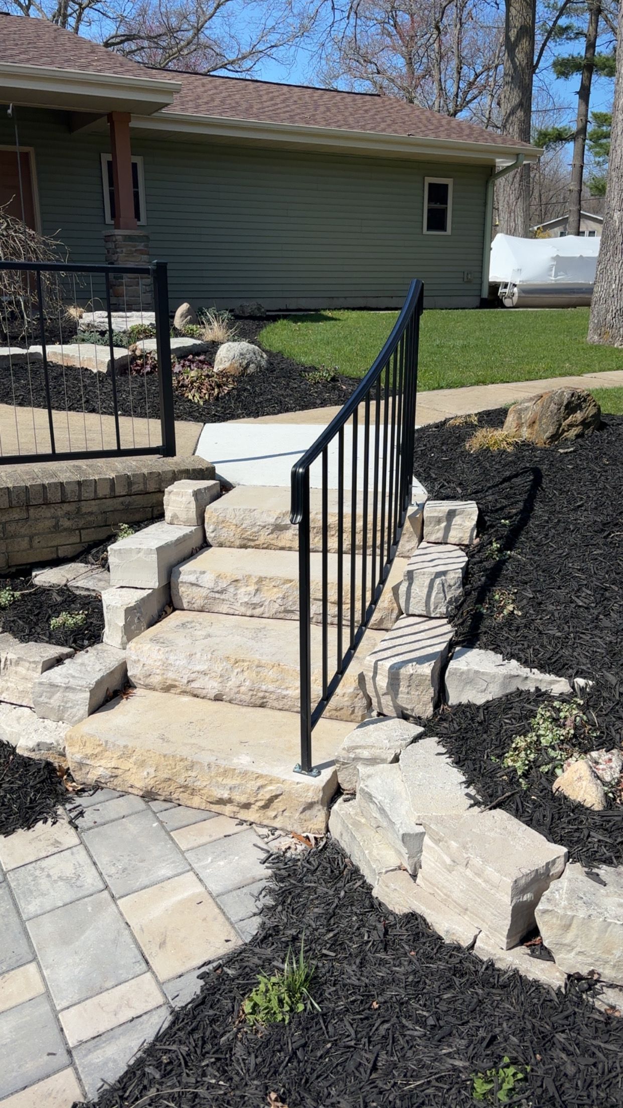 Stone steps with black metal railing leading to a house, surrounded by black mulch.