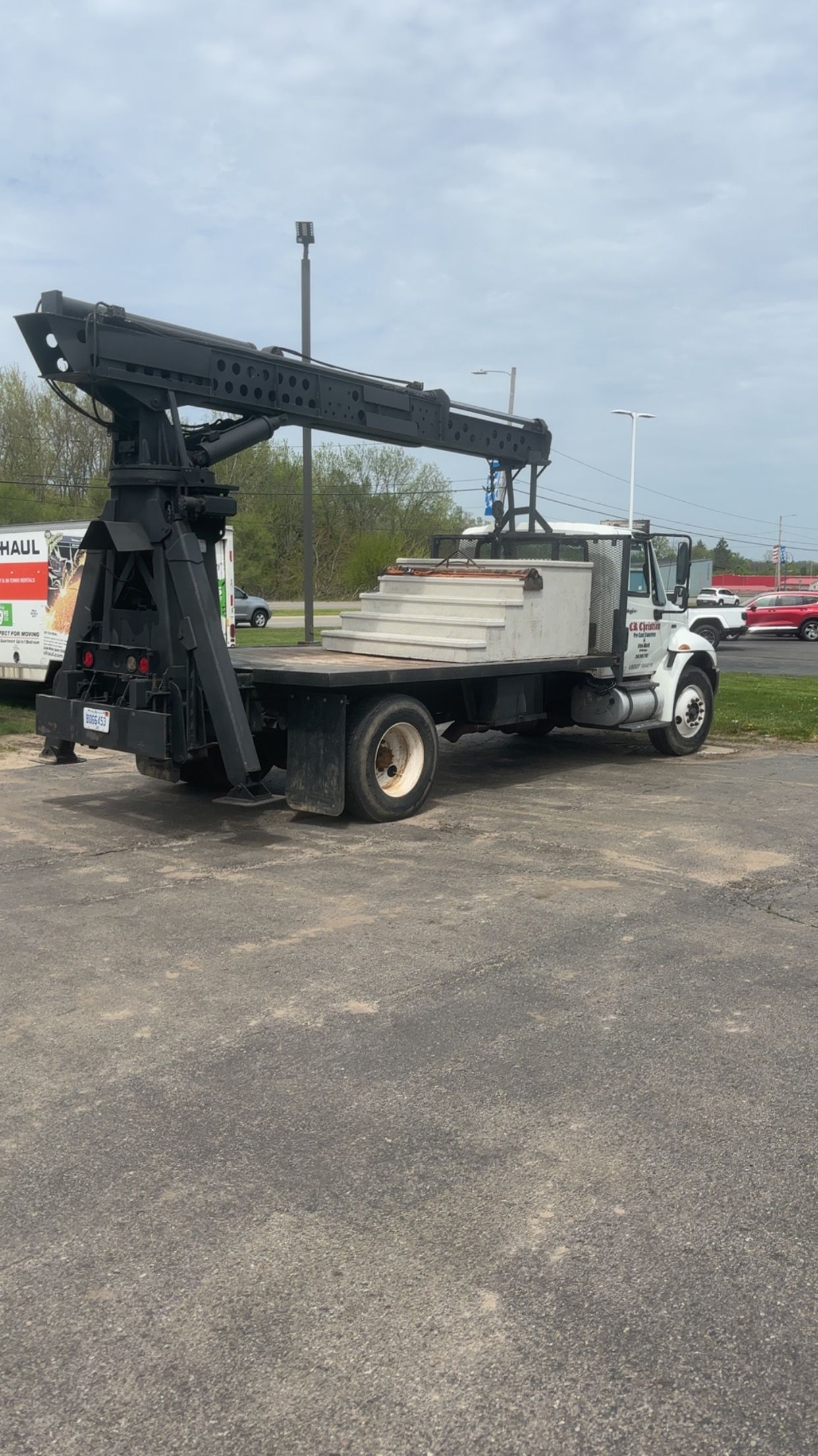 Flatbed truck with a large black crane arm, parked on asphalt. Overcast day.