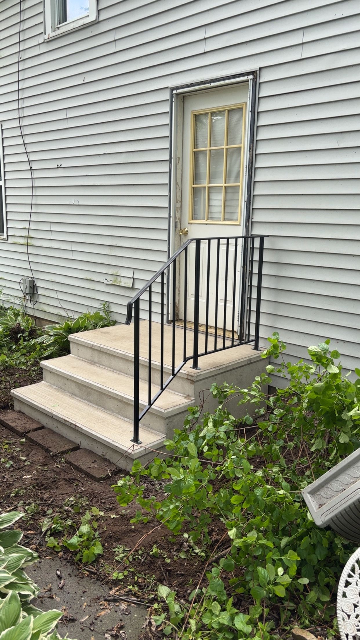 Concrete steps with black railing leading to a white door on the side of a weathered, light-colored building.