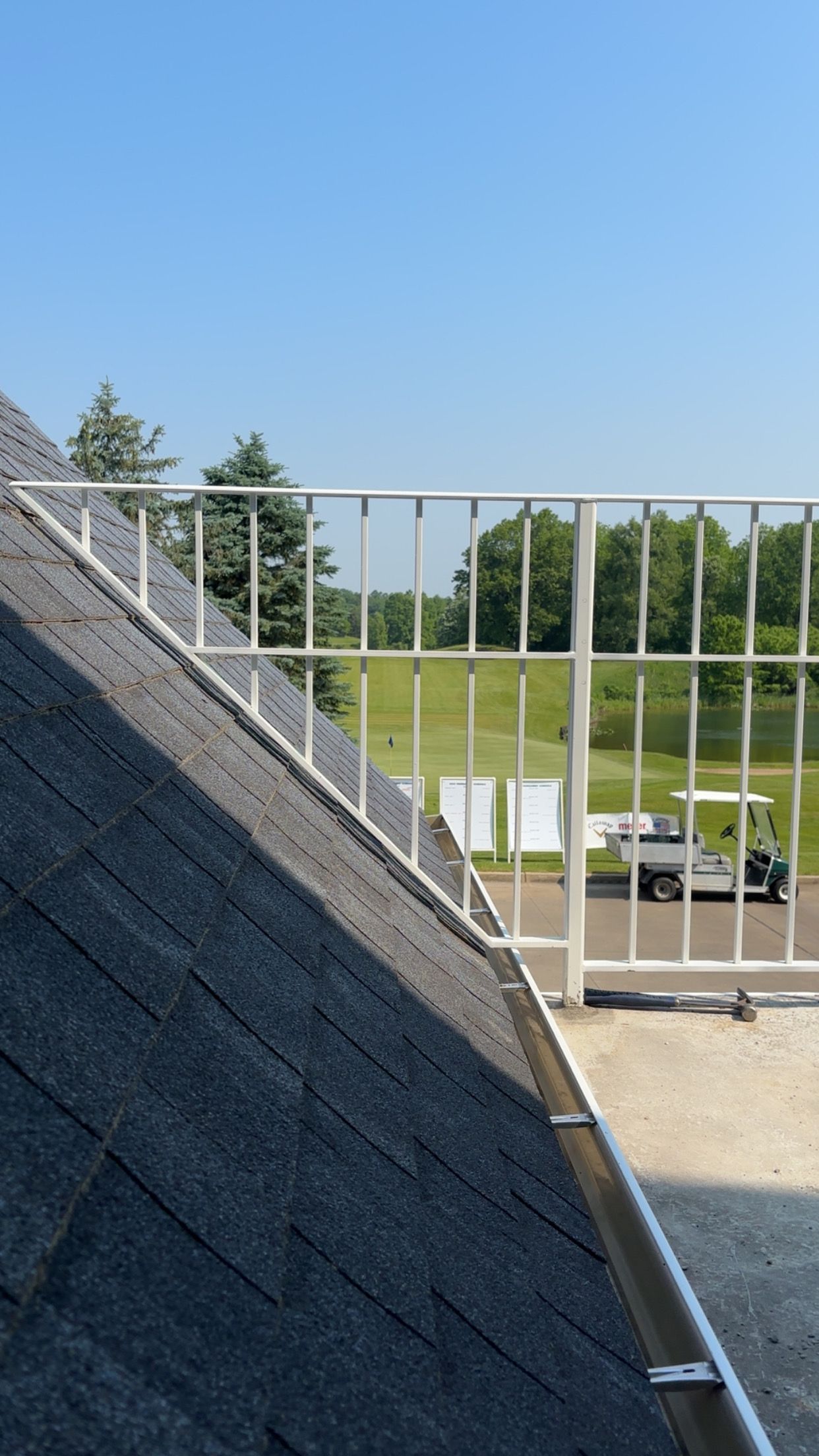 Rooftop with white railing overlooking a golf course. Sunny day with blue sky and golf cart.