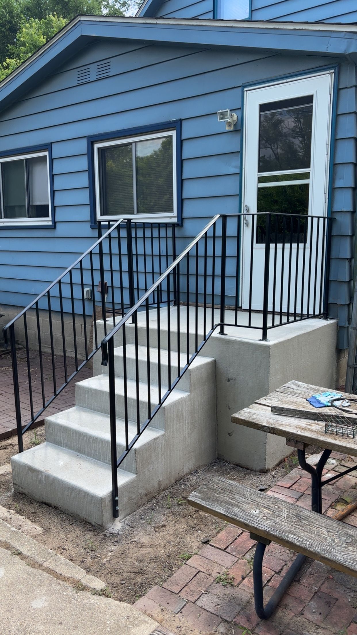 Blue house exterior with concrete steps, black railing, and a door.