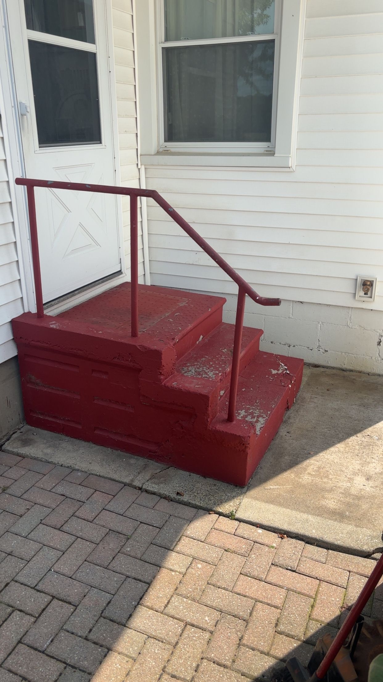 Red wooden steps with a handrail leading up to a white house entrance.