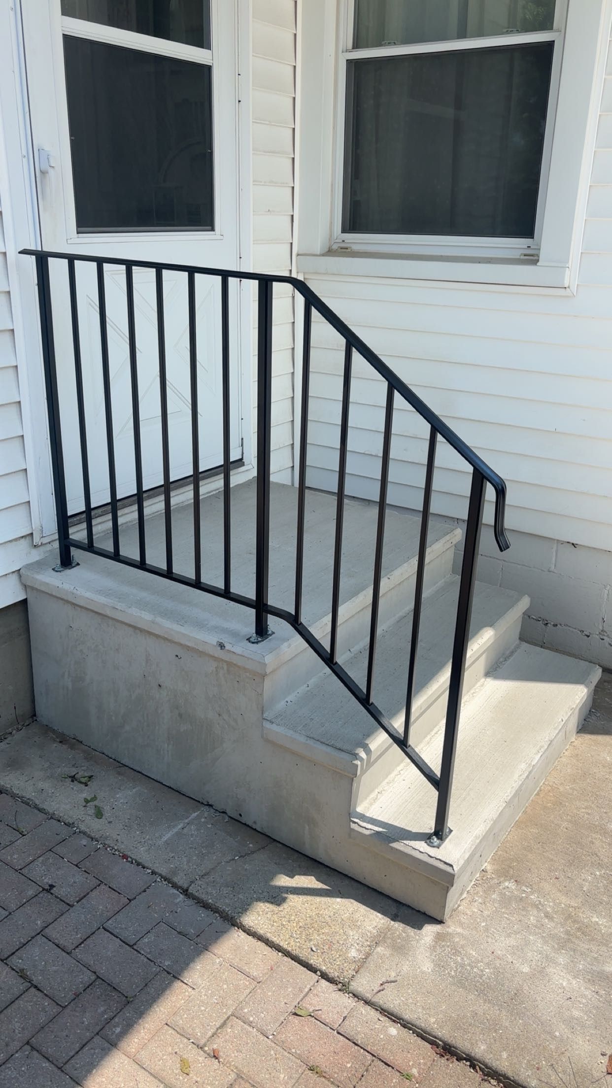 Exterior concrete steps with a black metal railing next to a white house.