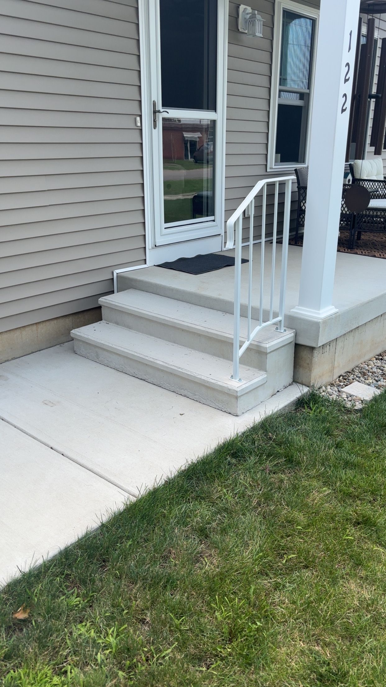 Concrete steps and railing leading to a house entrance with beige siding and a white screen door.