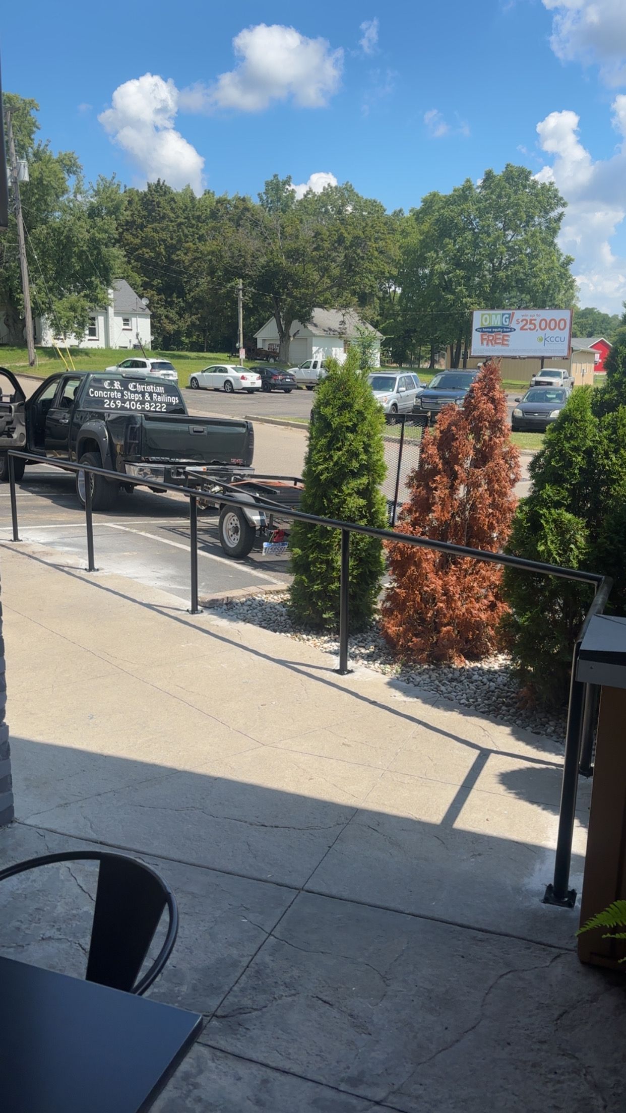 A sunny outdoor scene with a truck frame, trees, and parked cars under a blue sky.