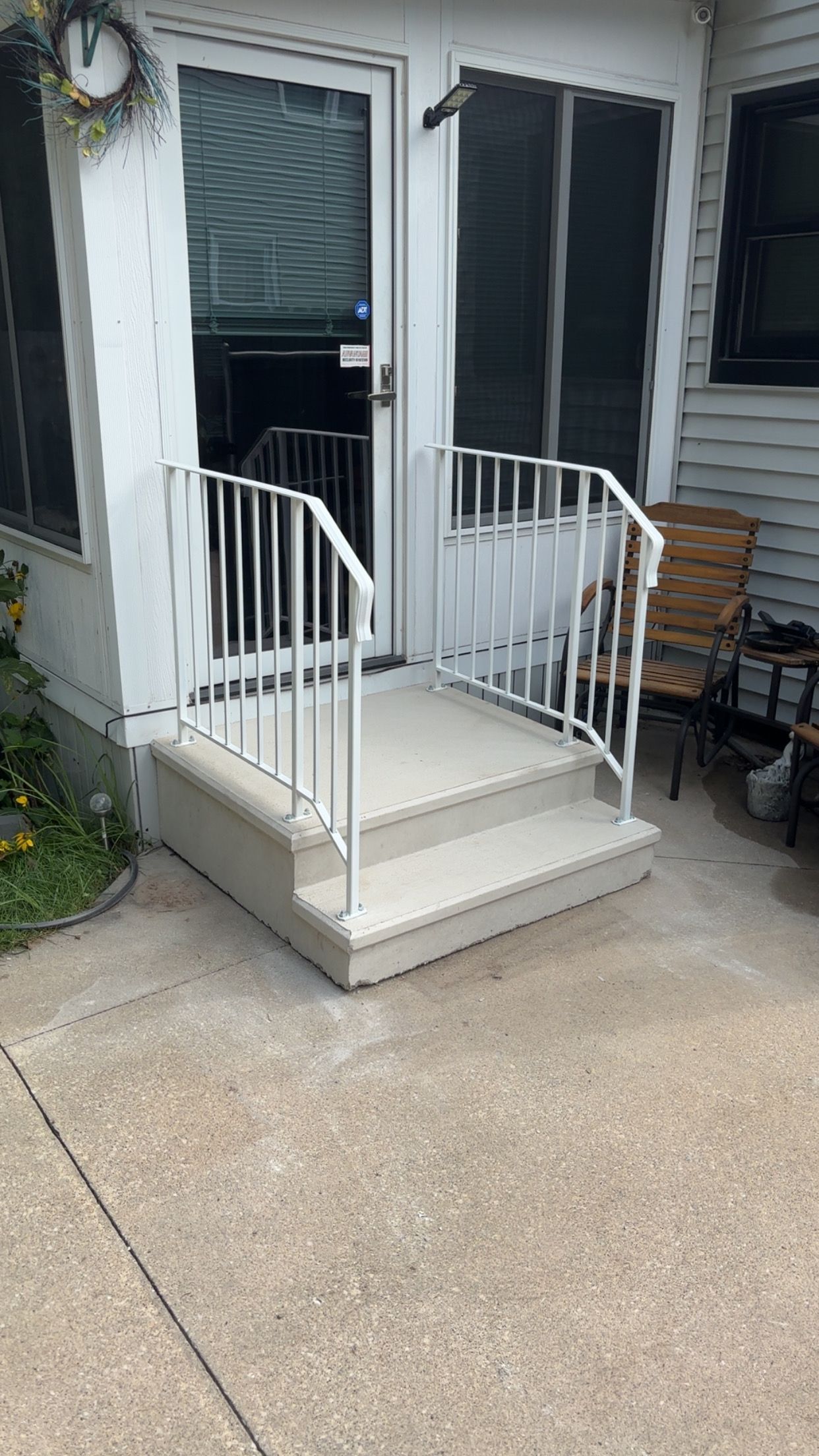 White railing surrounds concrete steps leading to a glass door.