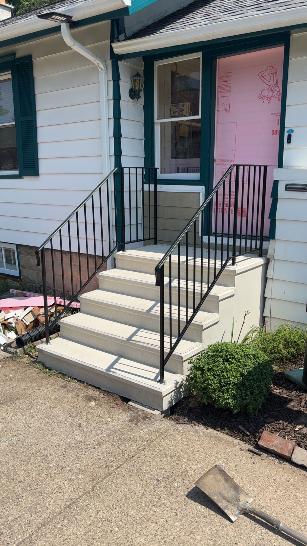 Front entrance of a house with concrete steps, black handrails, and a pink door.