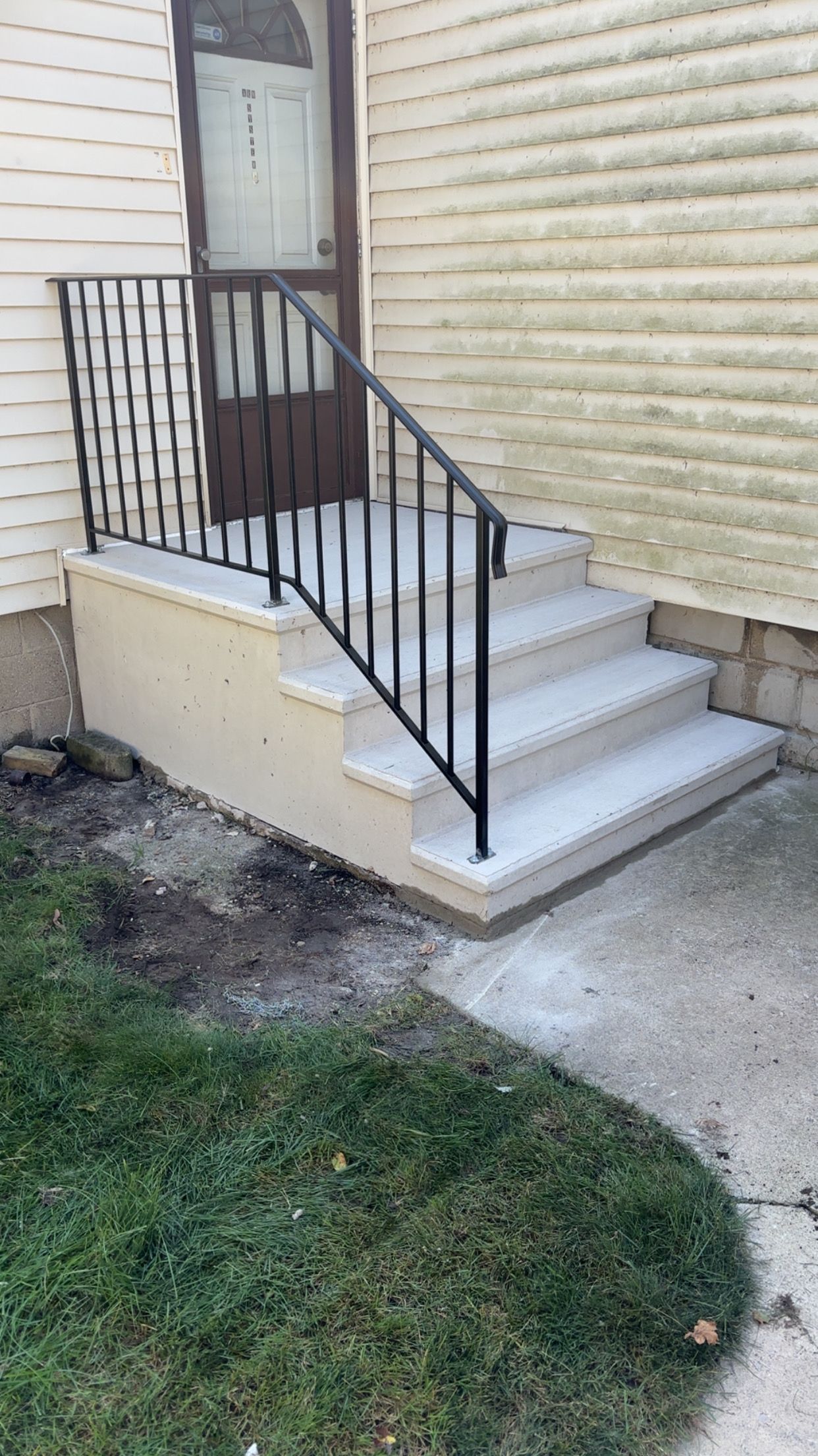 Exterior steps with black railing leading to a doorway. Concrete steps are gray, siding is off-white.
